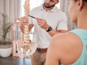 A chiropractor showing a woman a model of a human spine.